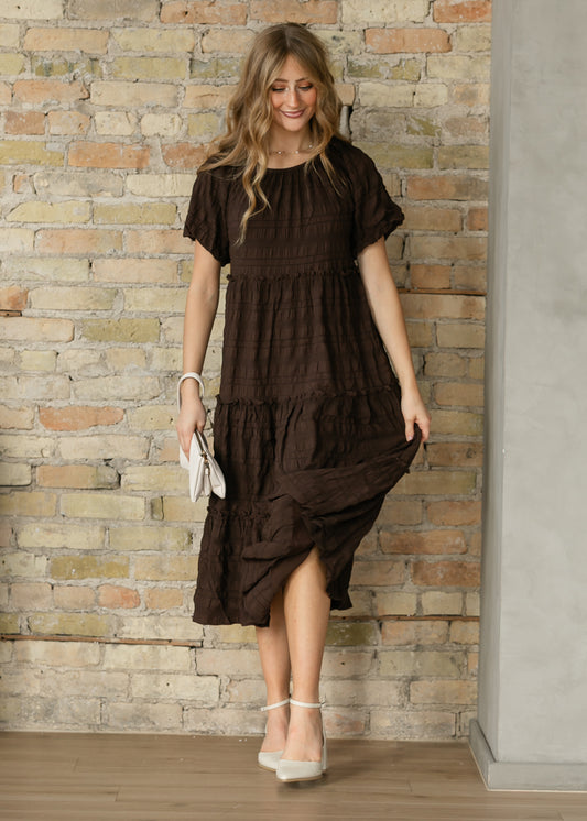 Model walking in the Serena Chocolate Brown Midi Dress, holding the ruffled skirt to show its movement.