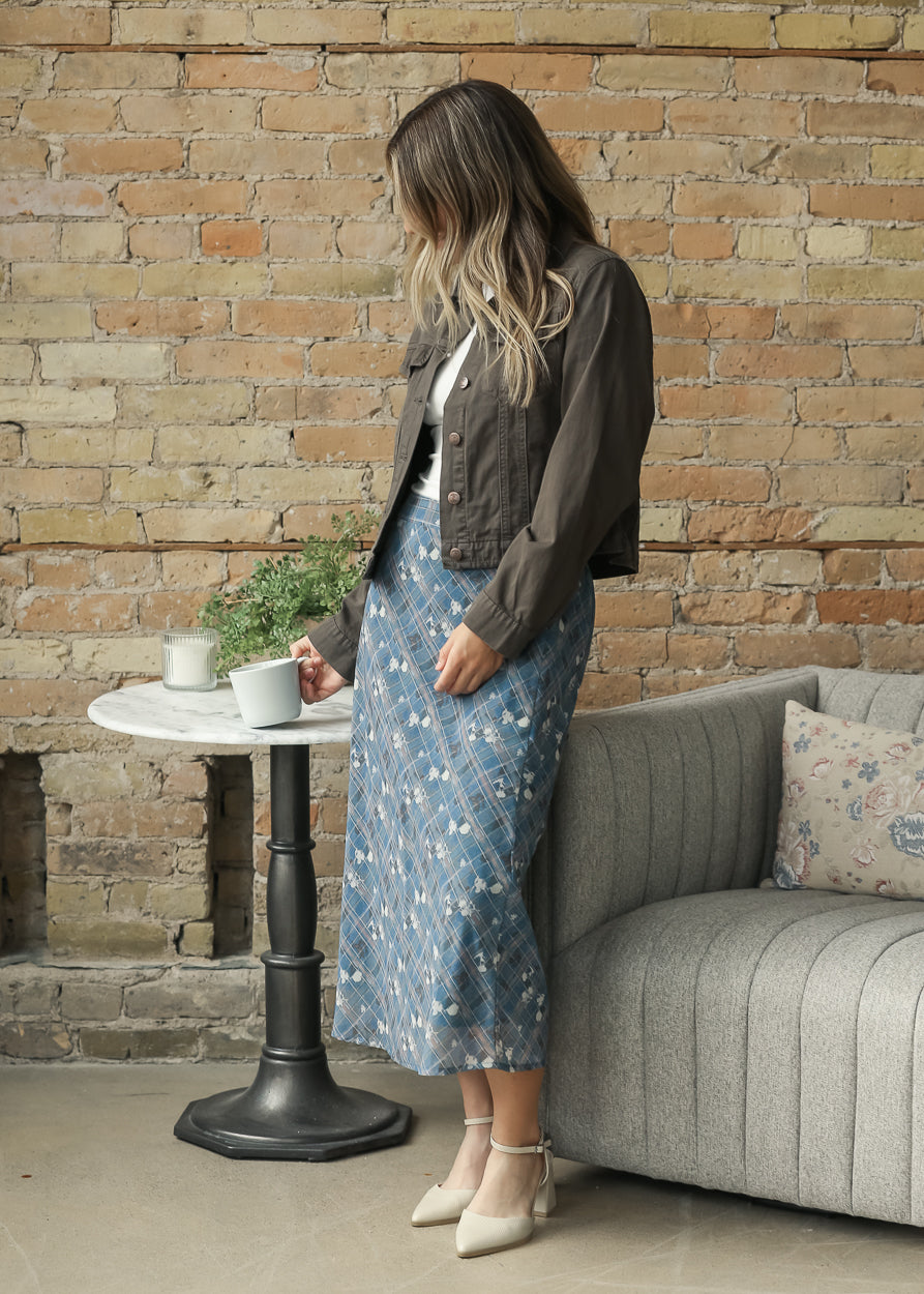 A woman wearing a dark brown cropped jacket, a blue floral midi skirt, and beige heels.