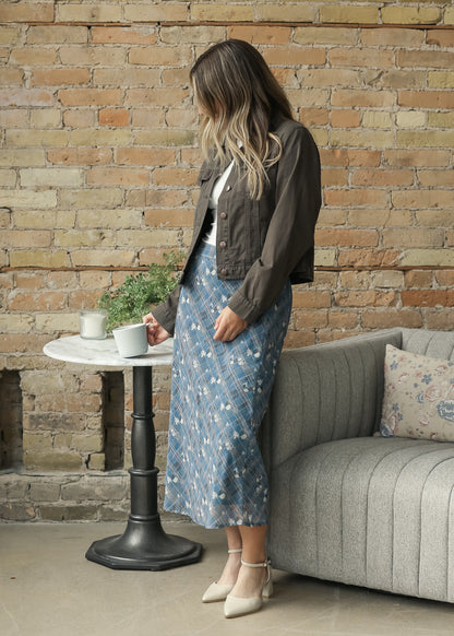 A woman wearing a dark brown cropped jacket, a blue floral midi skirt, and beige heels.