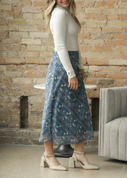 A woman wearing a white long-sleeve top and a blue floral midi skirt with white block-heel mules.