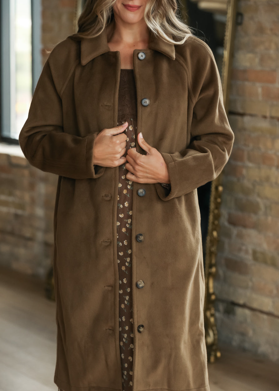 A woman wearing a brown long-sleeve button-front coat over a brown patterned dress.