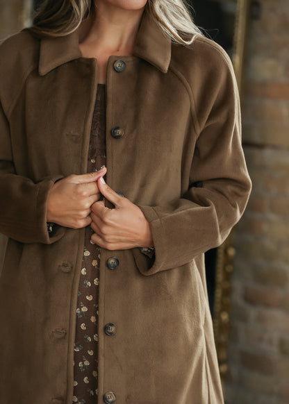 Close-up of a brown suede-like button-front coat over a patterned dress,.