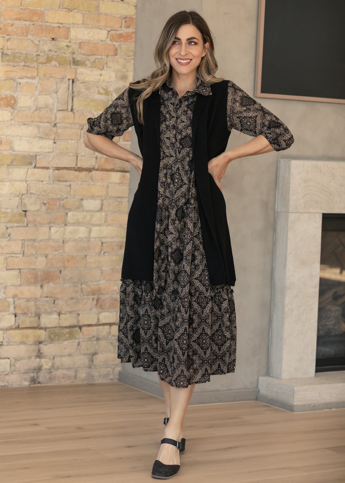 Black open-front cardigan with ribbed trim, styled over a black and taupe paisley dress.
