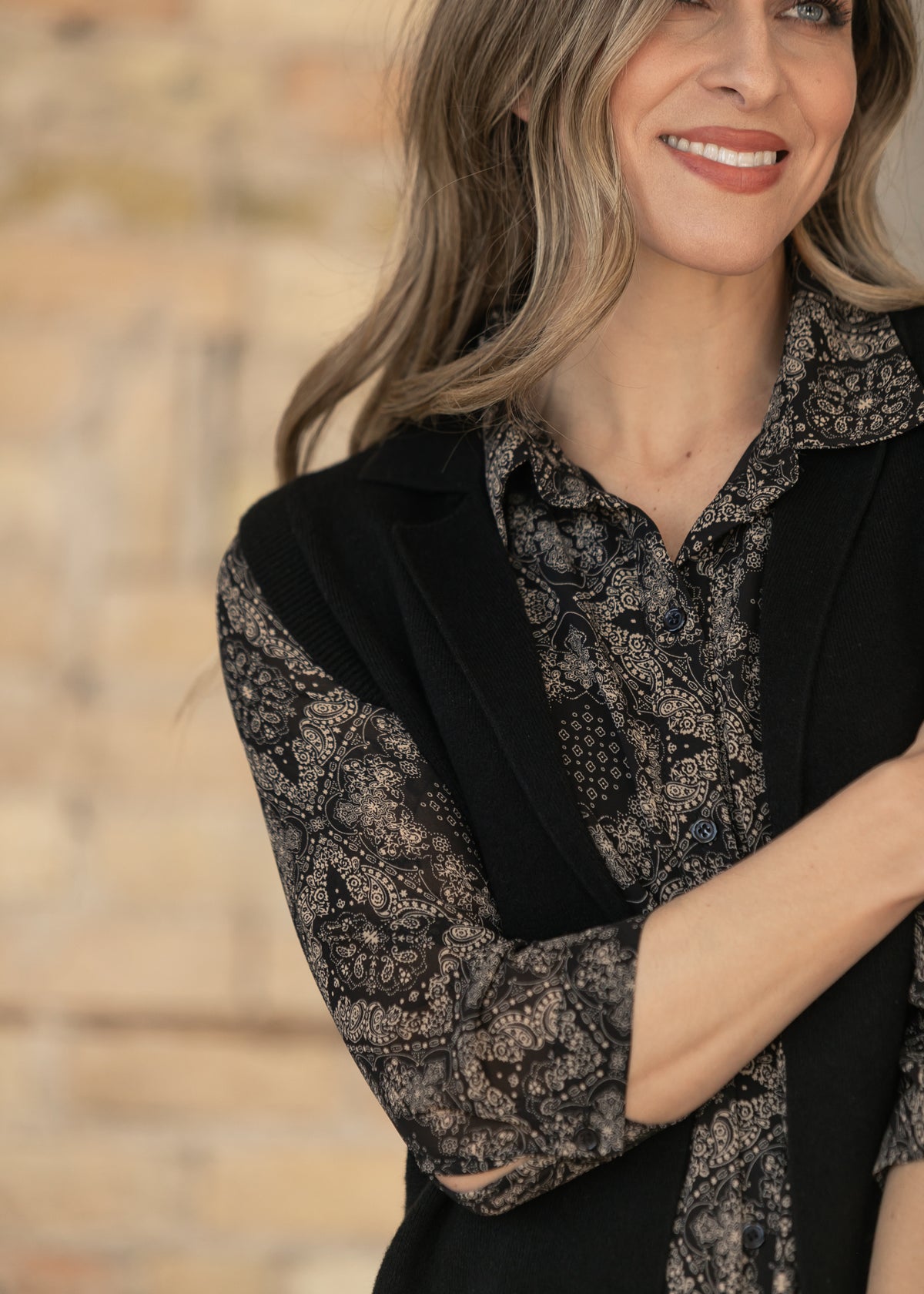 Close-up of black sleeveless cardigan showing ribbed armhole trim and knit texture over a paisley dress.
