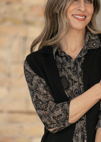 Close-up of black sleeveless cardigan showing ribbed armhole trim and knit texture over a paisley dress.