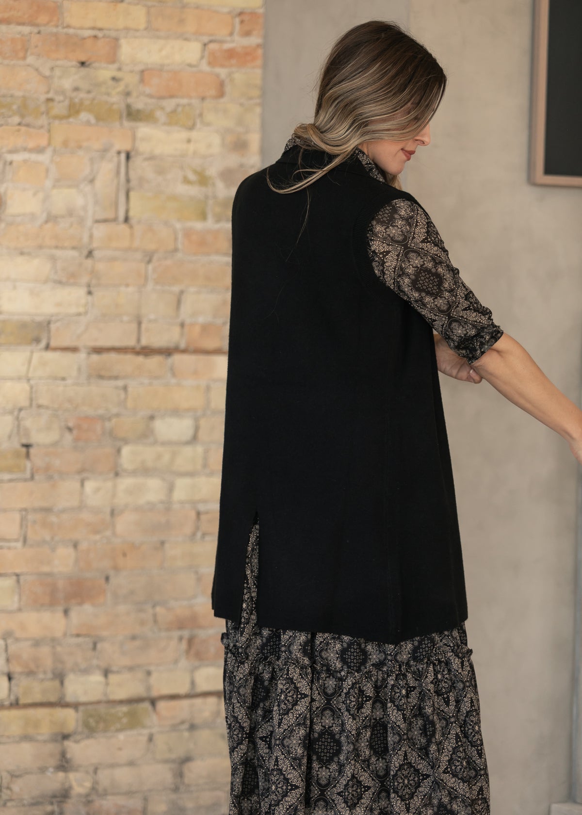Black open-front cardigan with ribbed trim, styled over a black and taupe paisley dress.