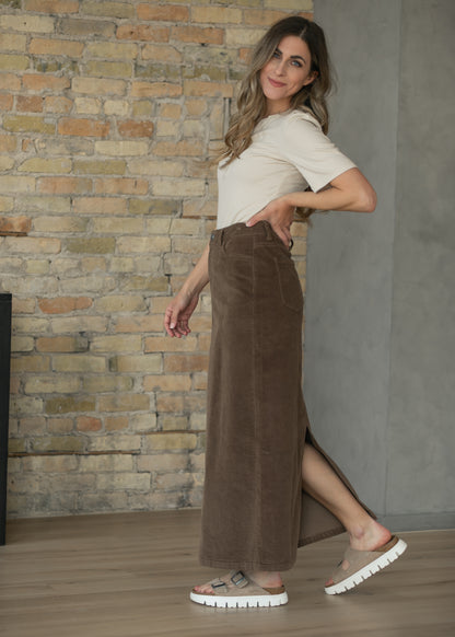 Brown corduroy maxi skirt shown in motion with a cream top and white sneakers.