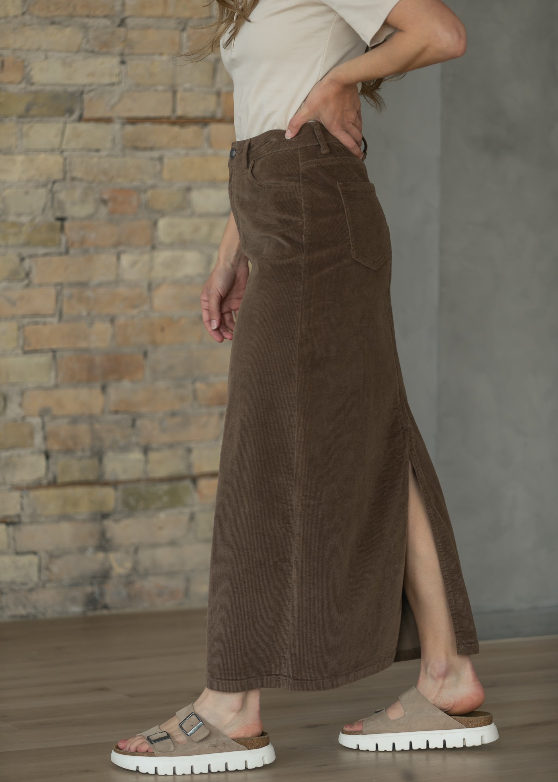 Side view of brown corduroy maxi skirt styled with a cream top and white sneakers.