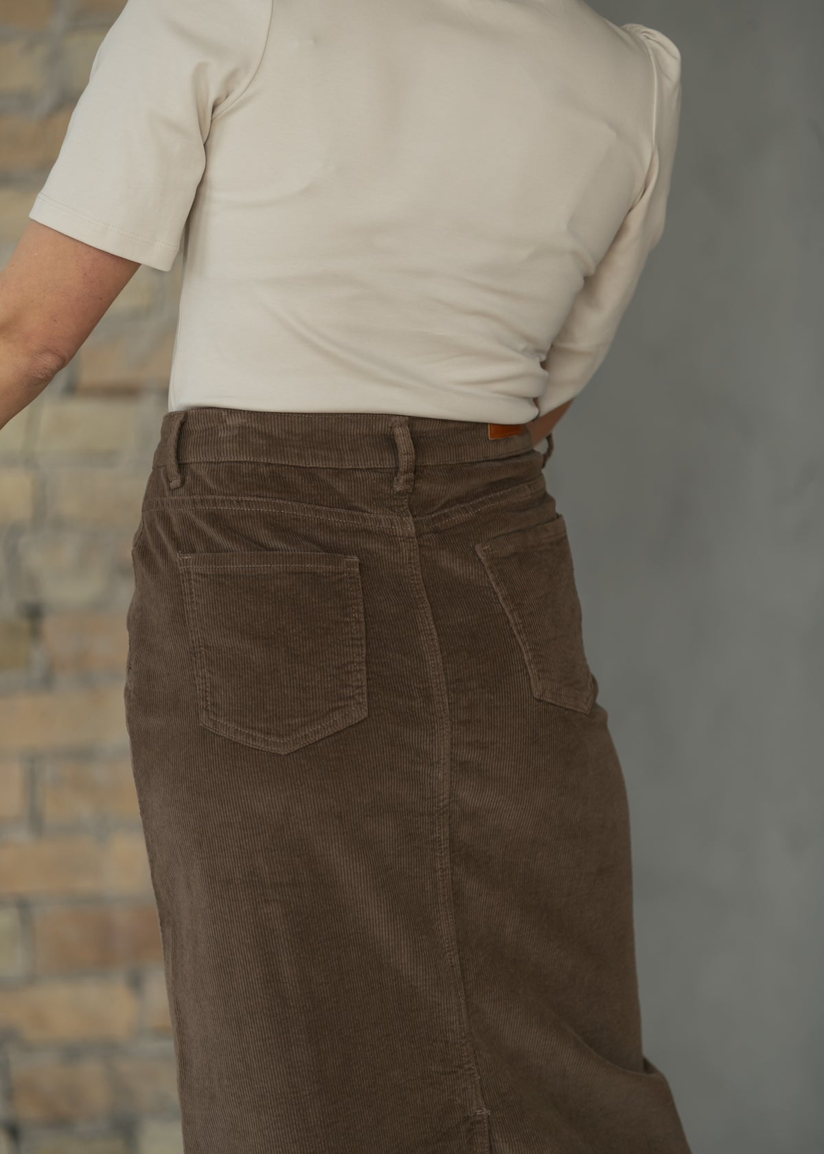 Close-up of brown corduroy maxi skirt with button closure, front pockets, belt loops, and textured fabric.
