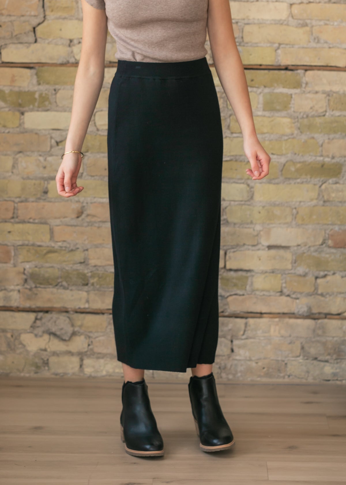 Person wearing a black knit skirt and black boots against a brick wall.