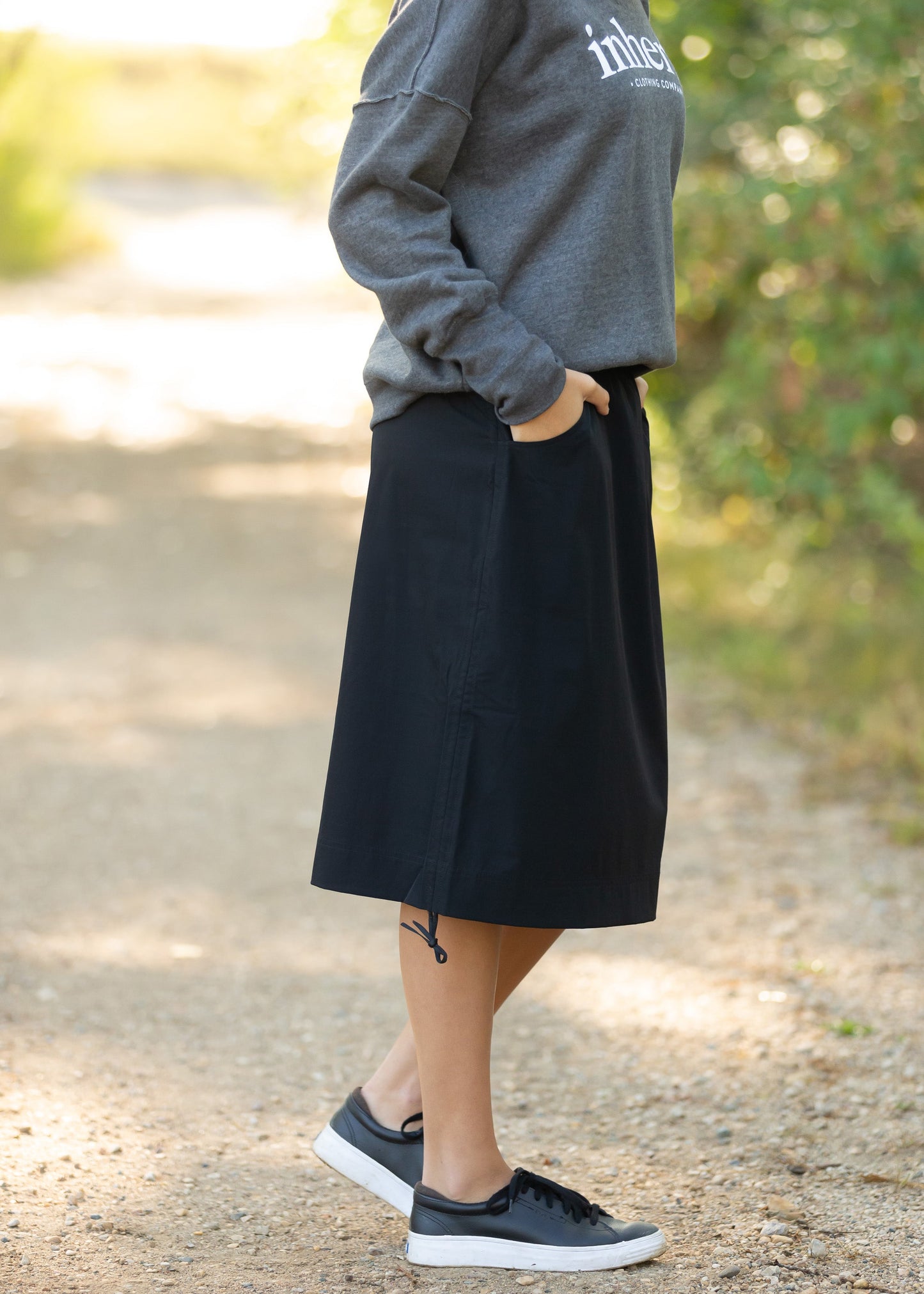 Andie Black Hiking Midi Skirt is a black athletic style midi length skirt with side pockets, a stretch waist, and draw strings at the hem.