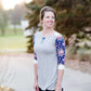 Woman wearing a raglan baseball style top. The shirt is gray with contrasting navy and pink floral sleeves.