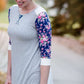 Woman wearing a raglan baseball style top. The shirt is gray with contrasting navy and pink floral sleeves.
