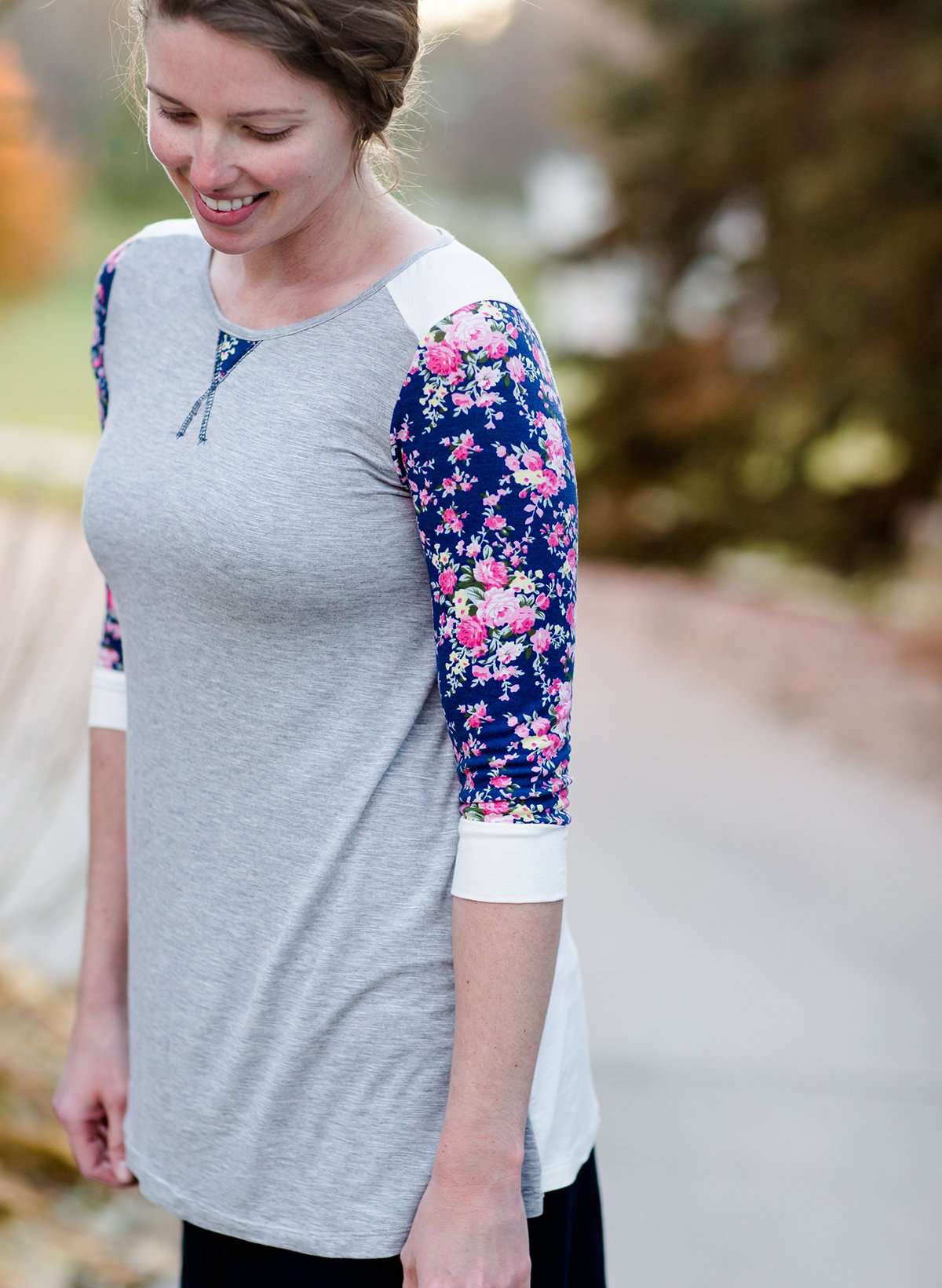 Woman wearing a raglan baseball style top. The shirt is gray with contrasting navy and pink floral sleeves.