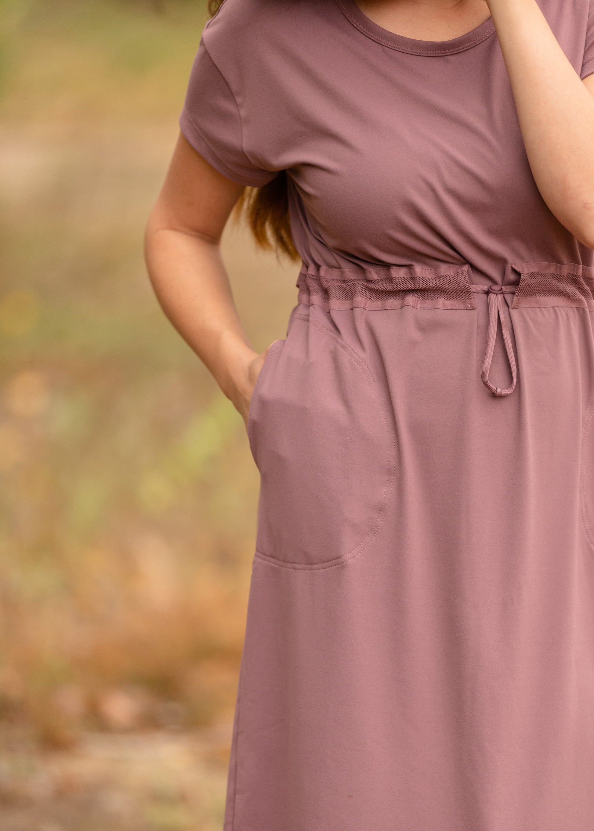 This is a Cinch Waist Athletic midi dress in a purpley taupe color that has a mesh detail and large side pockets. 