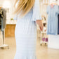 Woman wearing a modest baby blue and white striped midi dress with ruffles on the hem and sleeves