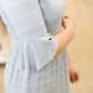 Woman wearing a modest baby blue and white striped midi dress with ruffles on the hem and sleeves