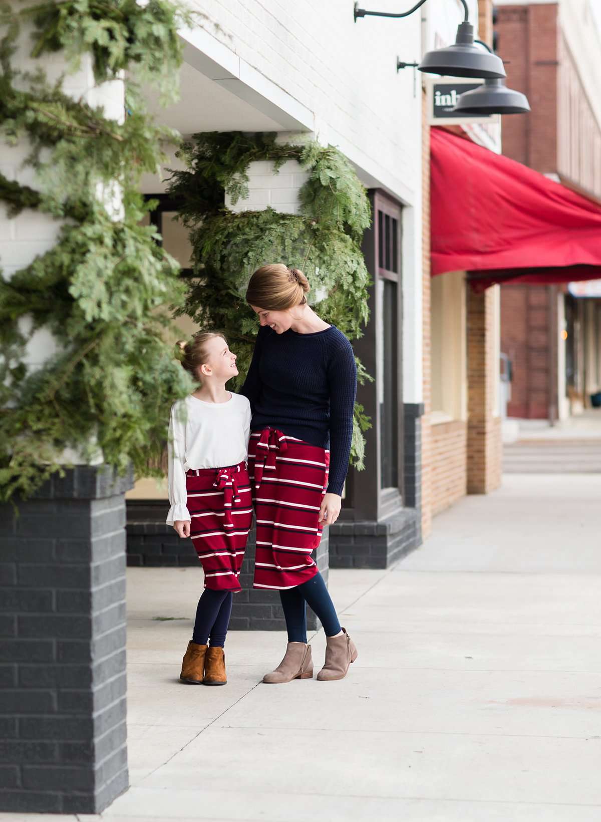 Woman wearing a modest mustard and burgandy striped midi skirt. This skirt has a fabric belt that is removable and is also mommy and me styled. This skirt is paired with tights and boots.
