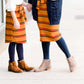 Woman wearing a modest mustard and burgandy striped midi skirt. This skirt has a fabric belt that is removable and is also mommy and me styled. This skirt is paired with tights and boots.