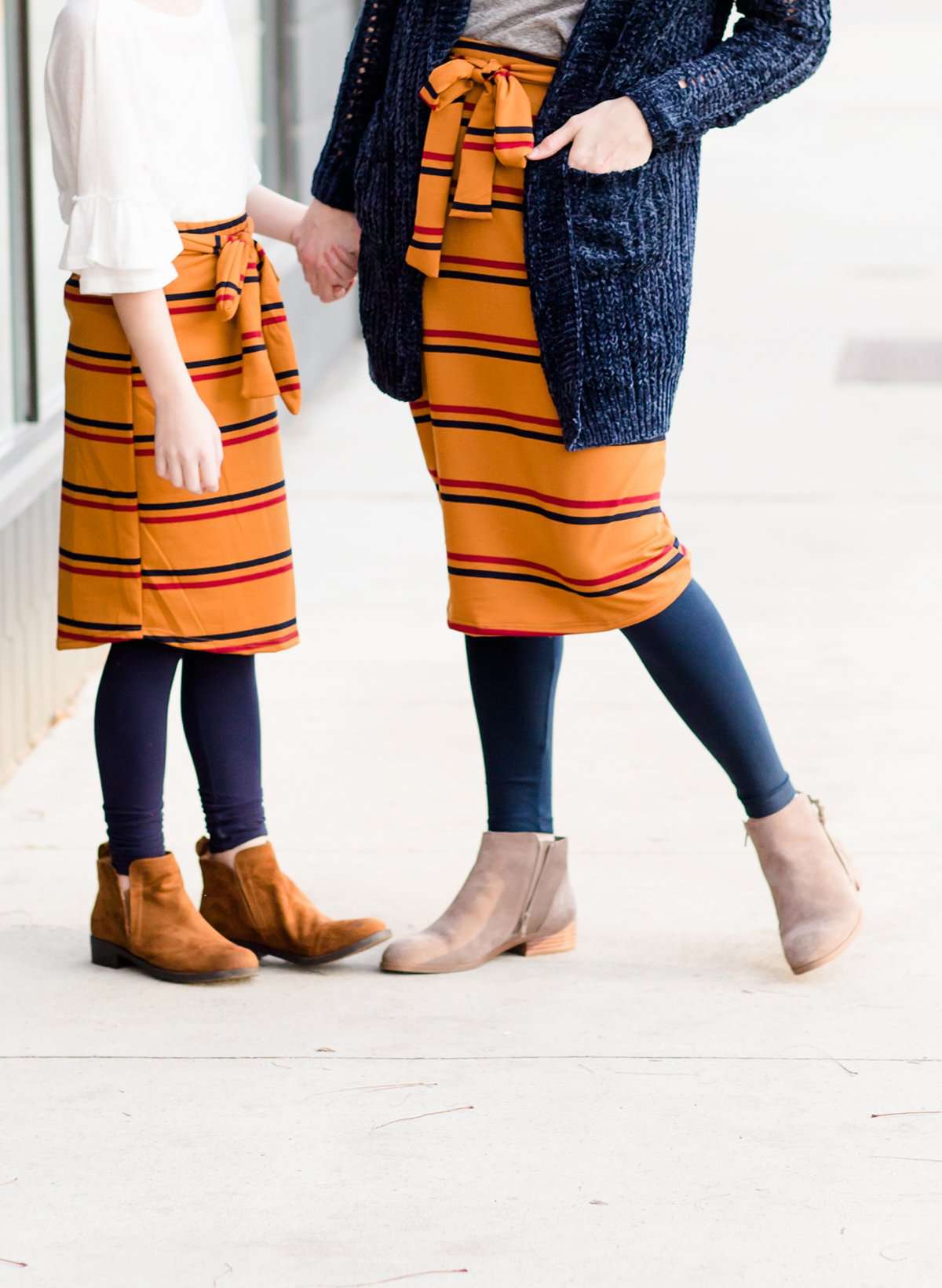 Woman wearing a modest mustard and burgandy striped midi skirt. This skirt has a fabric belt that is removable and is also mommy and me styled. This skirt is paired with tights and boots.