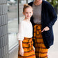 Woman wearing a modest mustard and burgandy striped midi skirt. This skirt has a fabric belt that is removable and is also mommy and me styled. This skirt is paired with tights and boots.
