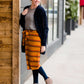 Woman wearing a modest mustard and burgandy striped midi skirt. This skirt has a fabric belt that is removable and is also mommy and me styled. This skirt is paired with tights and boots.