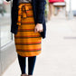Woman wearing a modest mustard and burgandy striped midi skirt. This skirt has a fabric belt that is removable and is also mommy and me styled. This skirt is paired with tights and boots.