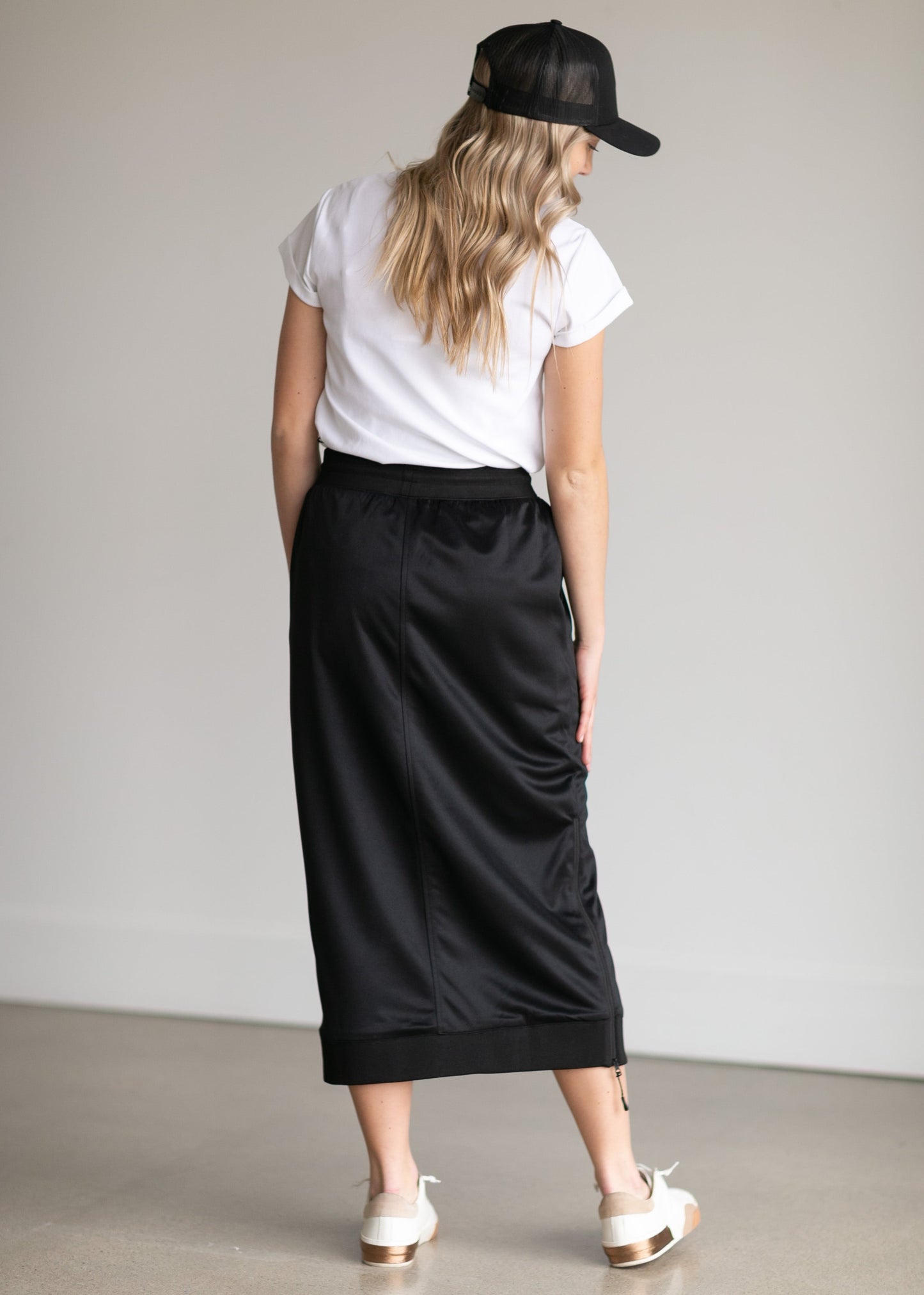 A black midi skirt with a drawstring waist, ribbed hem, pockets, and bottom side zipper.