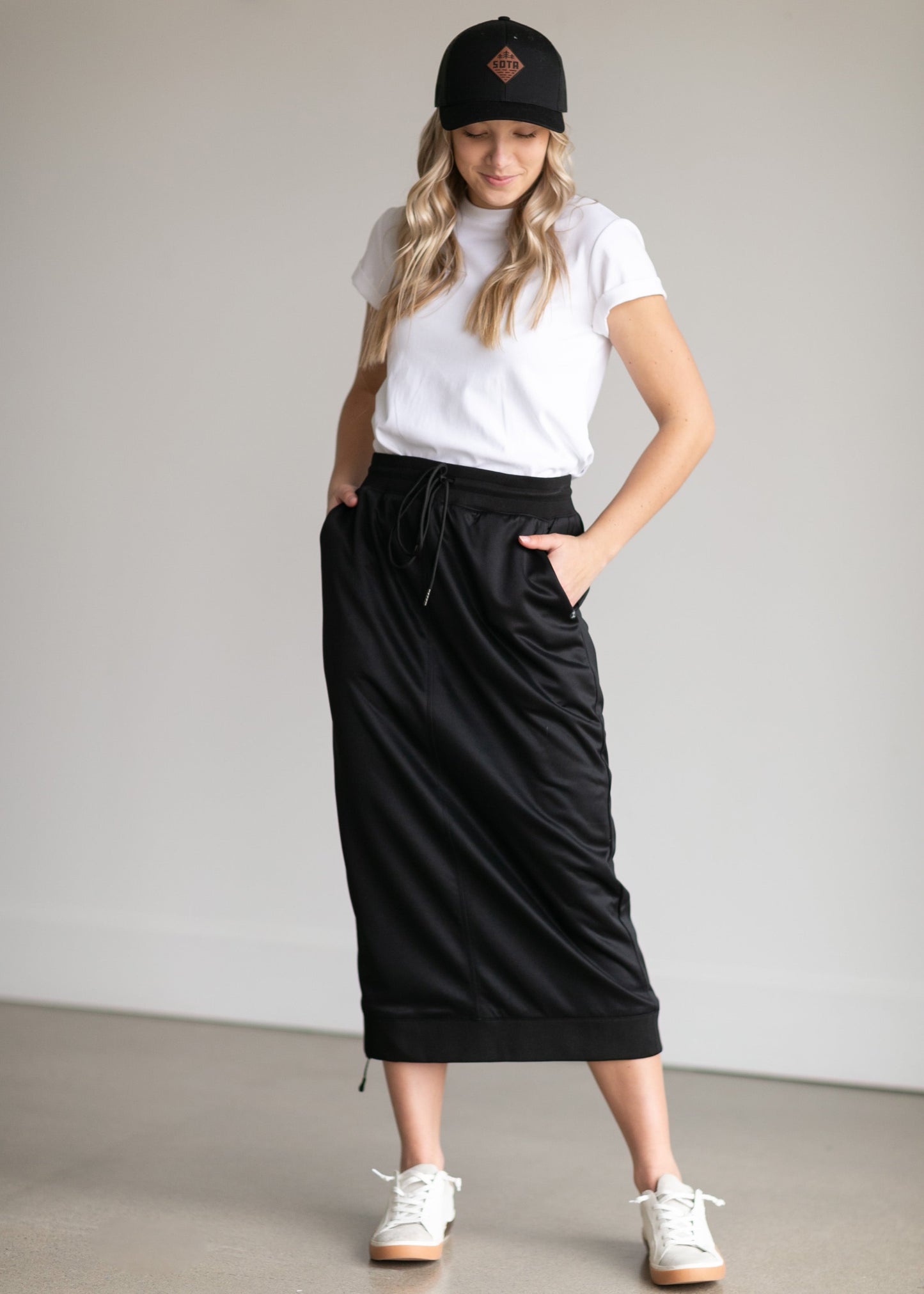 A black midi skirt with a drawstring waist, ribbed hem, pockets, and bottom side zipper.