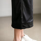 A black midi skirt with a drawstring waist, ribbed hem, pockets, and bottom side zipper.