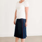 Woman wearing a dark indigo wash below the knee skirt that has red piping along the sides. She also is wearing a white tee shirt and tan sneakers.