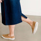 Woman wearing a dark indigo wash below the knee skirt that has red piping along the sides. She also is wearing a white tee shirt and tan sneakers.