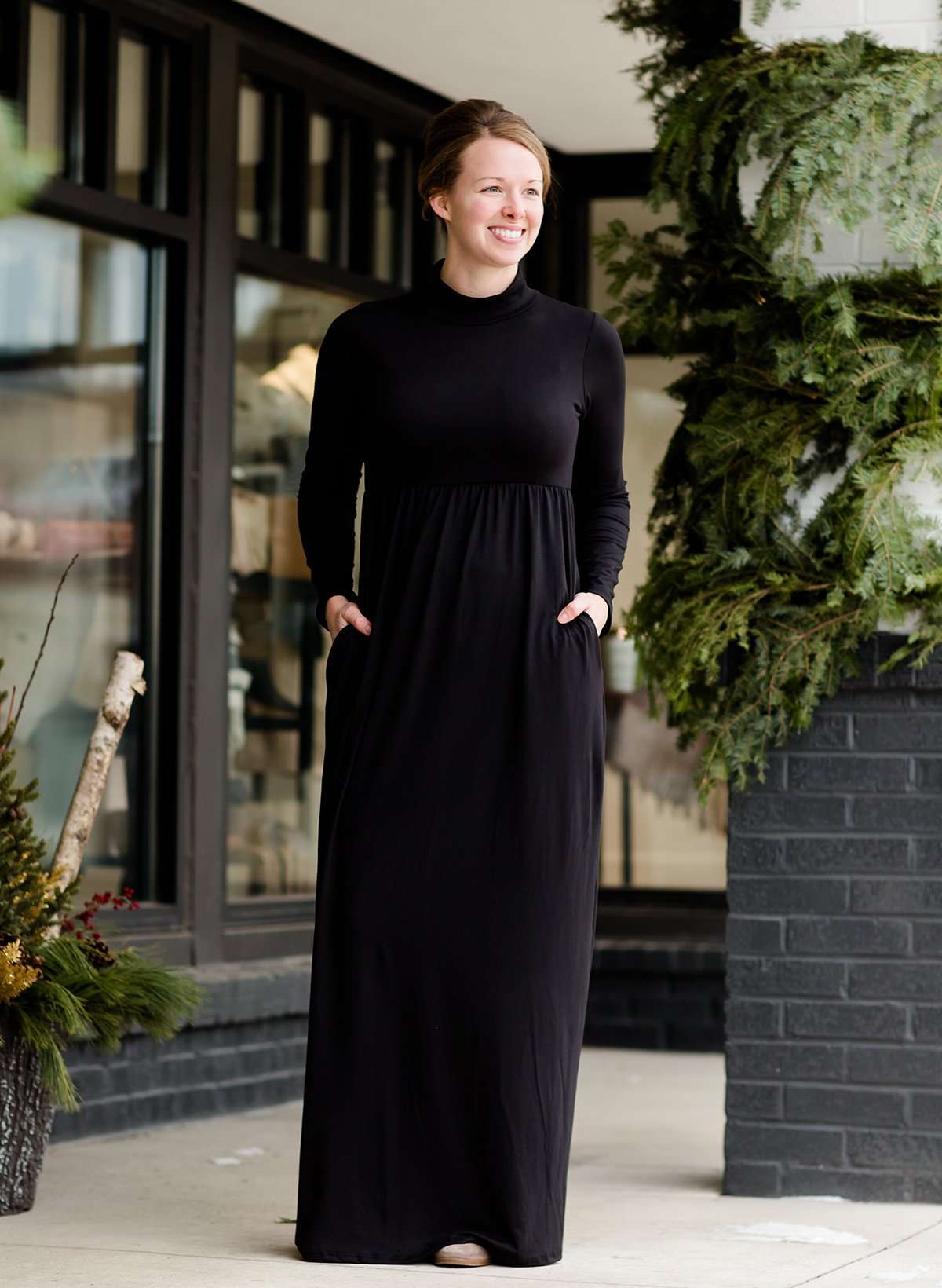 Woman wearing a black turtle neck maxi dress with pockets and a buffalo check vest standing outside of Inherit Clothing Company