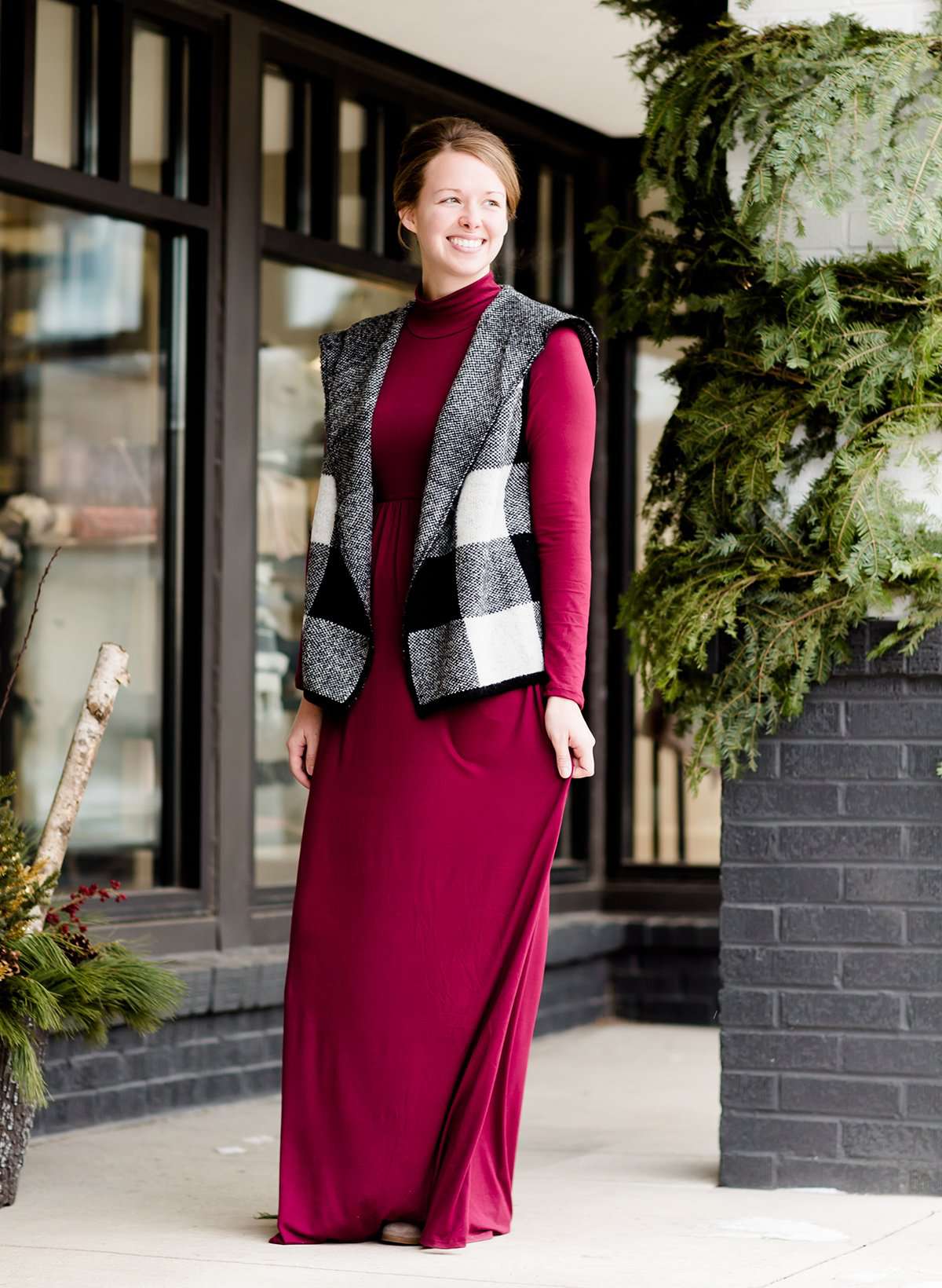 Woman wearing a Burgundy turtle neck maxi dress with pockets and a buffalo check vest standing outside of Inherit Clothing Company