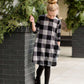 Young girl wearing a black and white buffalo check midi dress. This dress has 3/4 sleeves and front pockets. It is paired with black leggings and black booties.