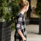 Young girl wearing a black and white buffalo check midi dress. This dress has 3/4 sleeves and front pockets. It is paired with black leggings and black booties.