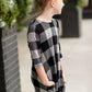 Young girl wearing a black and white buffalo check midi dress. This dress has 3/4 sleeves and front pockets. It is paired with black leggings and black booties.