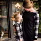 Young girl wearing a black and white buffalo check midi dress. This dress has 3/4 sleeves and front pockets. It is paired with black leggings and black booties.