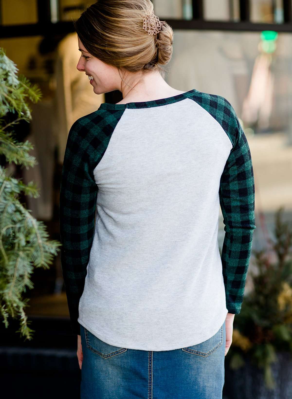Woman wearing a black and green buffalo check sleeve raglan top paired with a long modest jean skirt standing outside of Inherit Clothing Company!