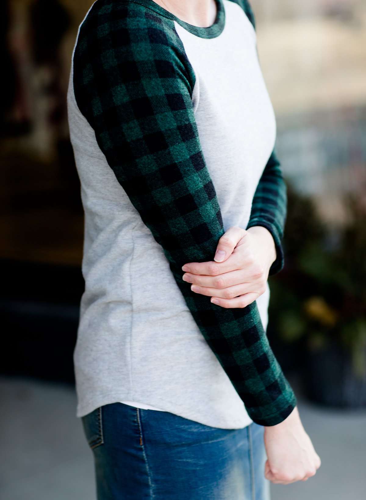 Woman wearing a black and green buffalo check sleeve raglan top paired with a long modest jean skirt standing outside of Inherit Clothing Company!
