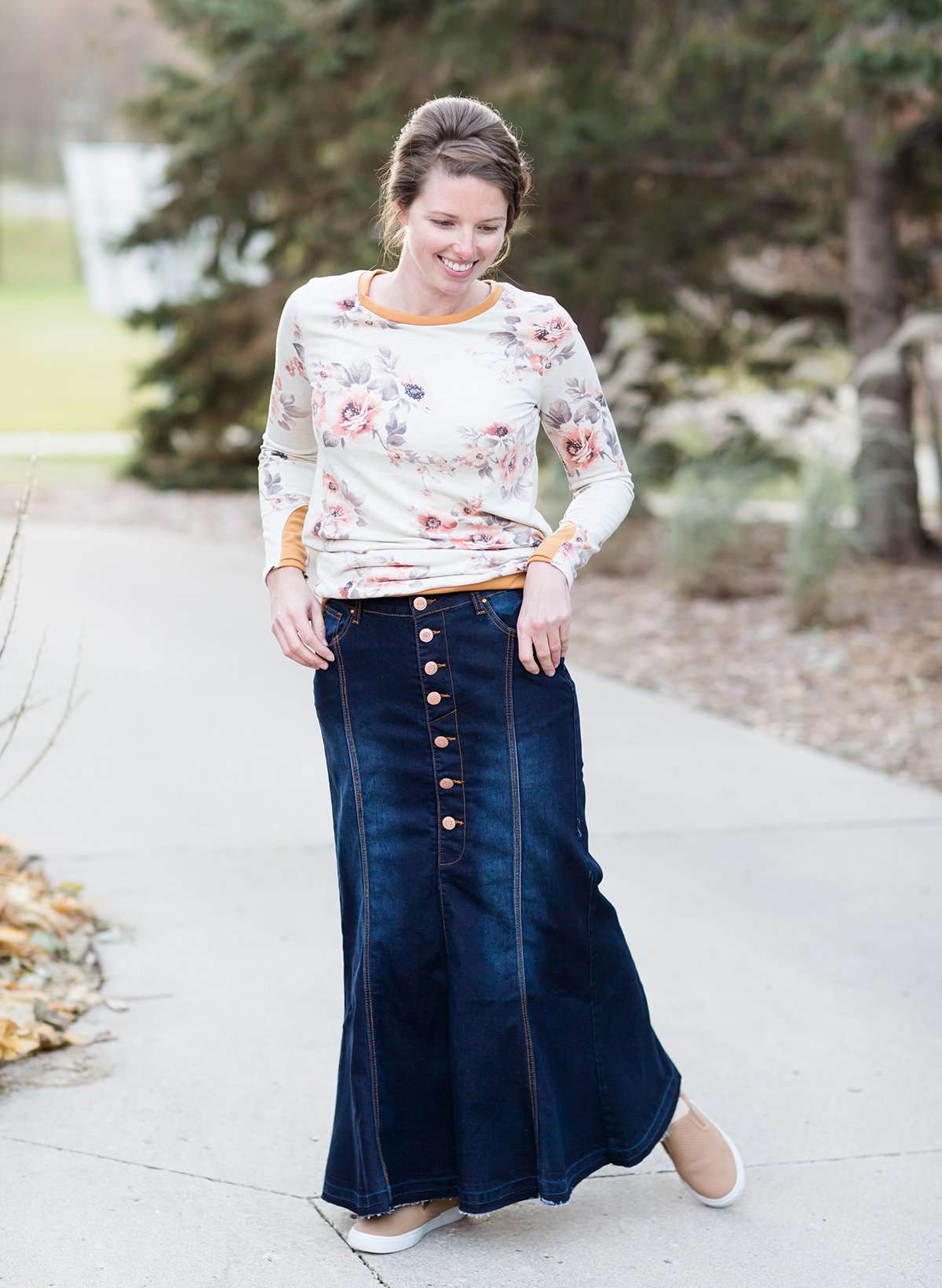 Woman wearing a long denim skirt without a slit that has buttons up the front and is a flare, a-line style.