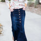Woman wearing a long denim skirt without a slit that has buttons up the front and is a flare, a-line style.