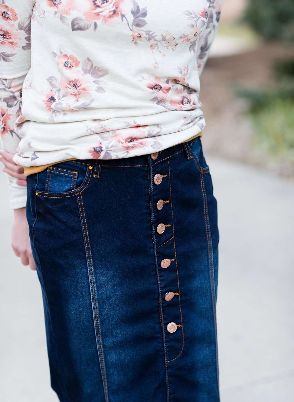 Woman wearing a long denim skirt without a slit that has buttons up the front and is a flare, a-line style.