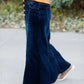 Woman wearing a long denim skirt without a slit that has buttons up the front and is a flare, a-line style.