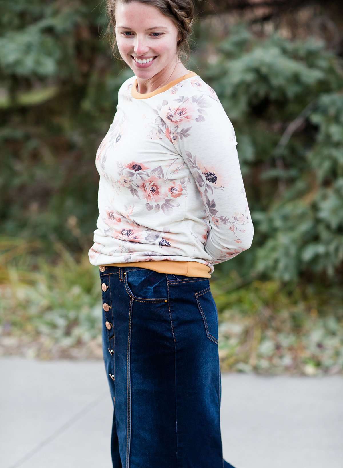 Woman wearing a long denim skirt without a slit that has buttons up the front and is a flare, a-line style.