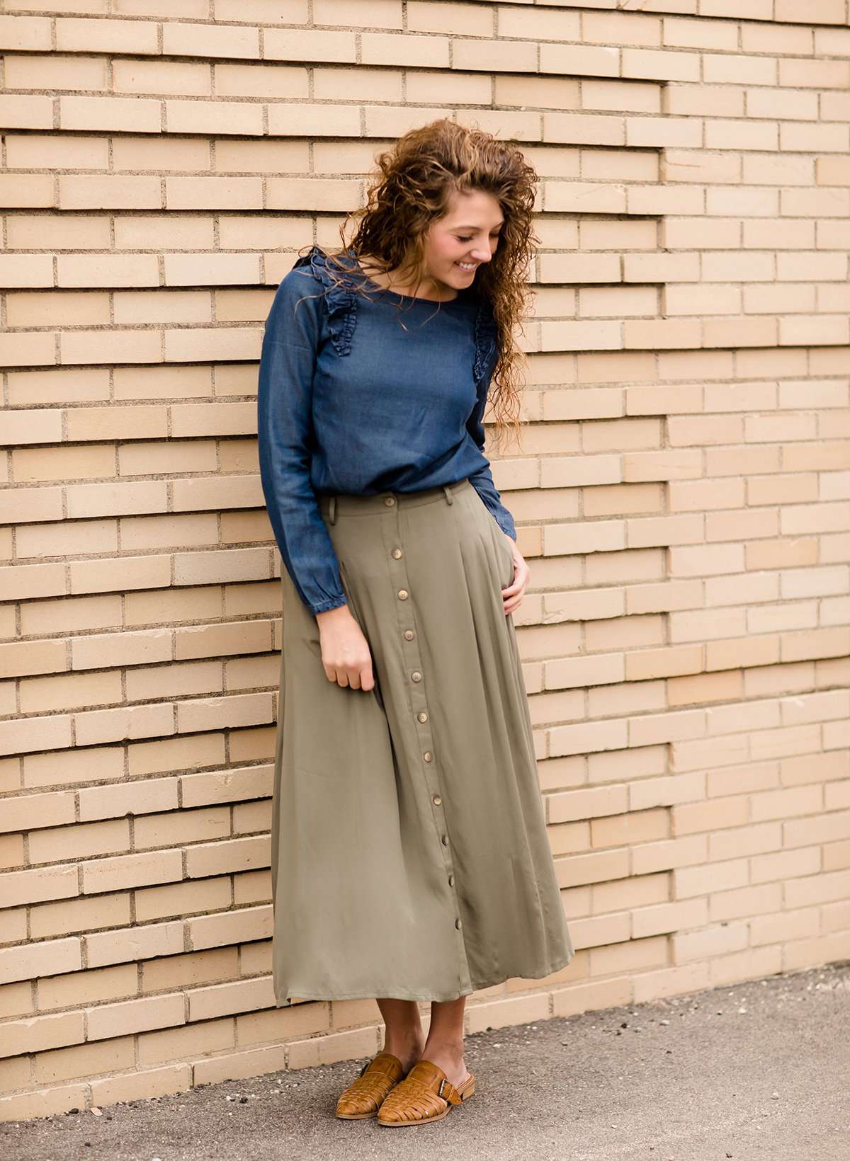 Woman wearing a lightweight ankle-length olive skirt with buttons up the front.