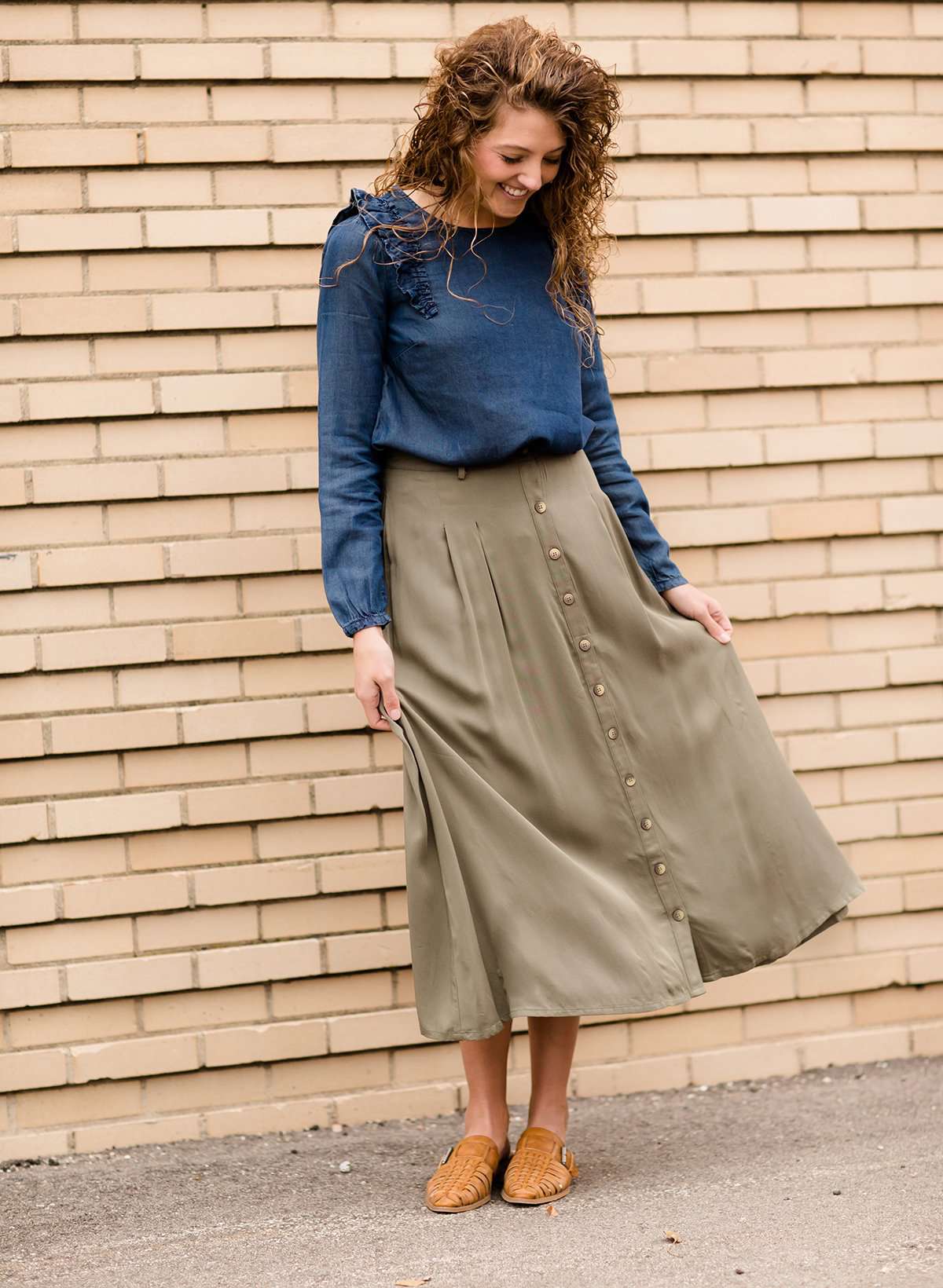 Woman wearing a lightweight ankle-length olive skirt with buttons up the front.