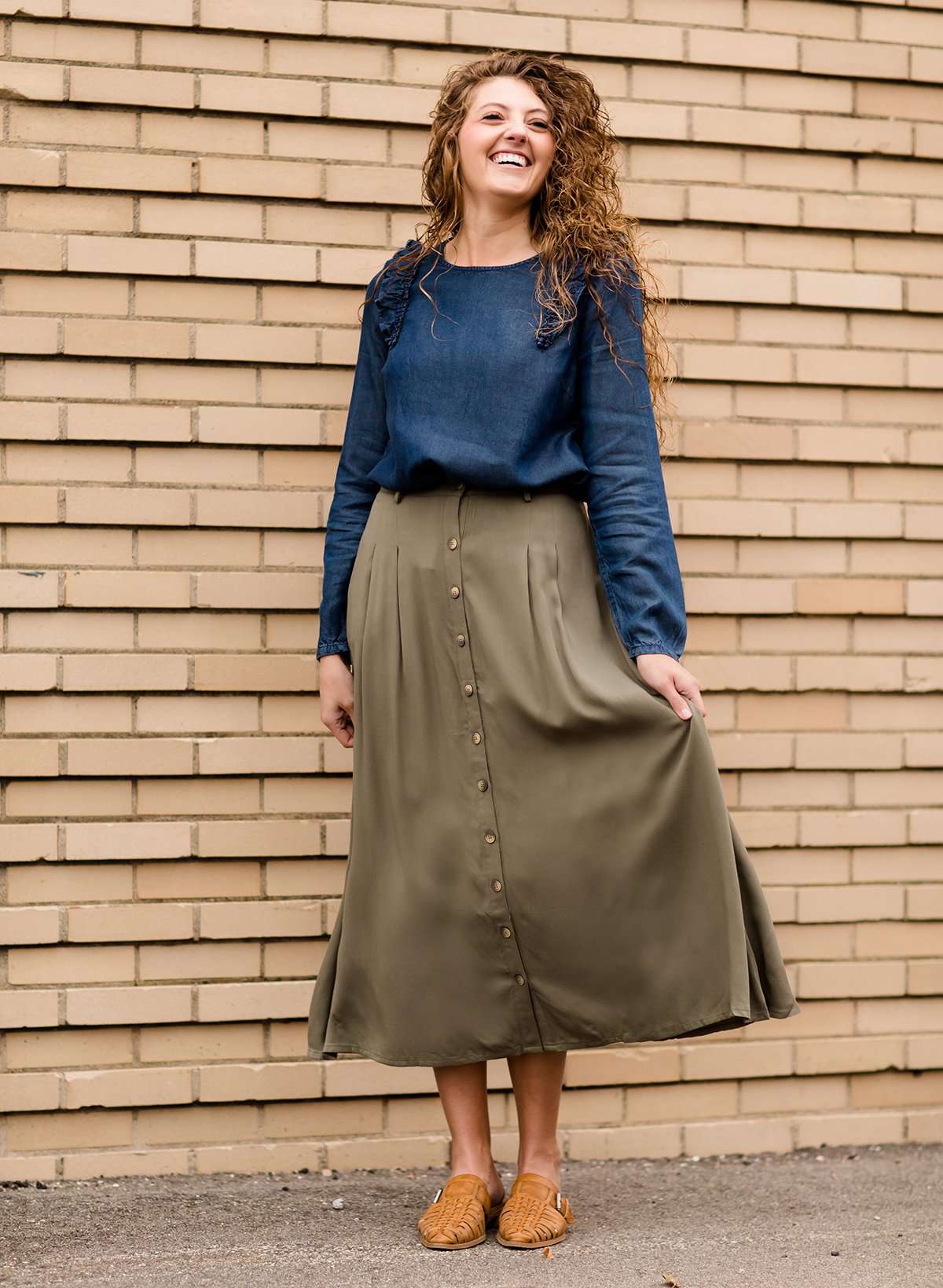 Woman wearing a lightweight ankle-length olive skirt with buttons up the front.