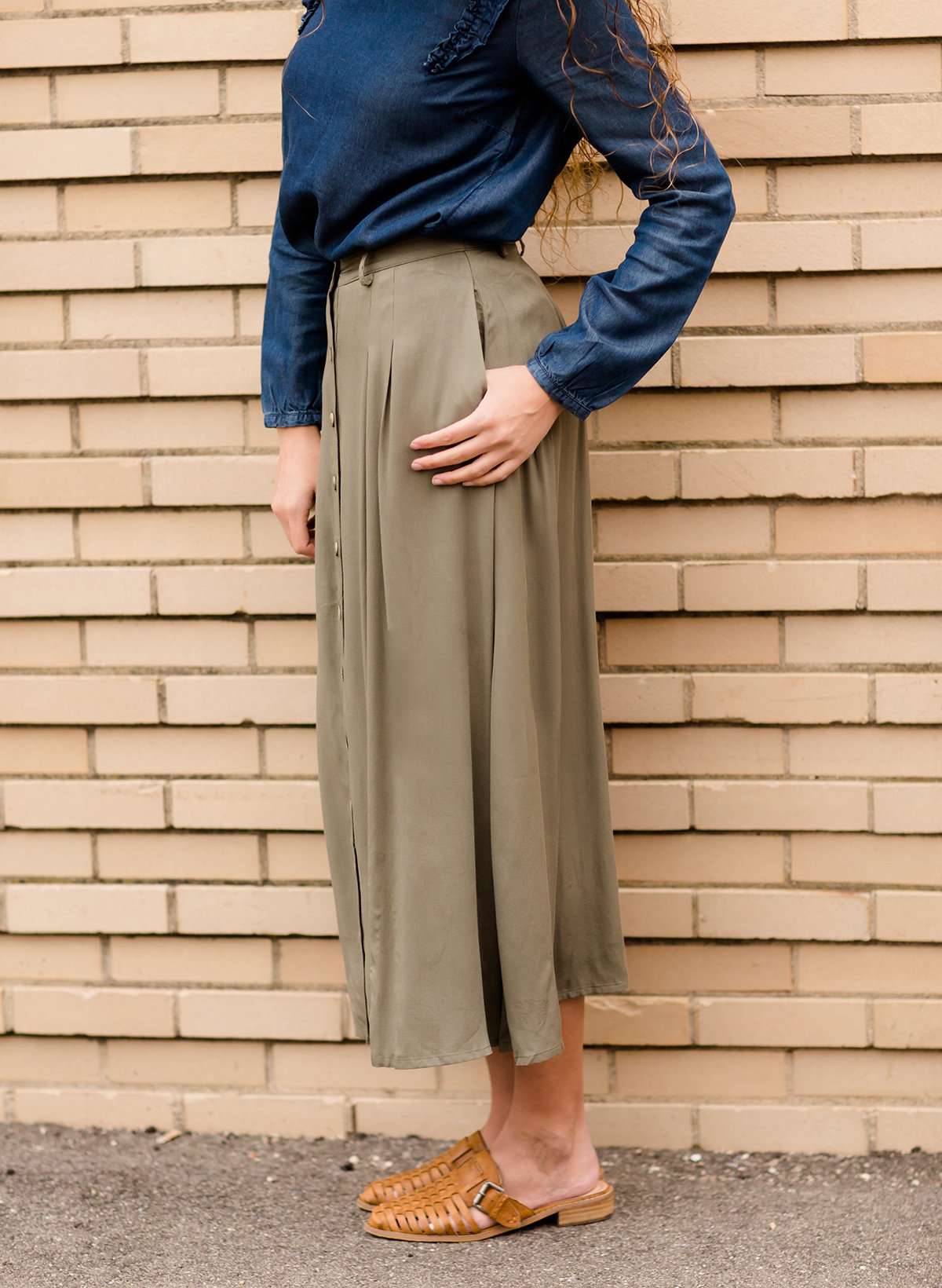 Woman wearing a lightweight ankle-length olive skirt with buttons up the front.