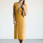Woman wearing a ribbed mustard midi dress with faux wood buttons.